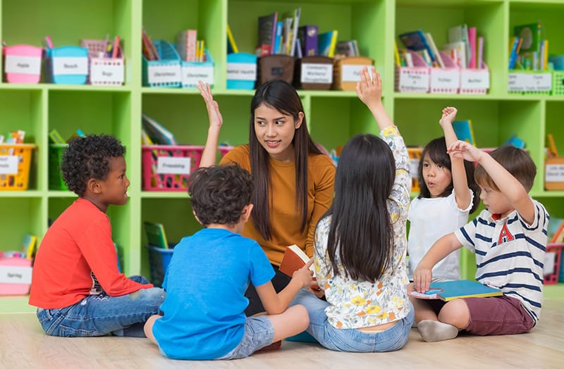 group of kids raise hand in prek class in florida with teacher at center Asian female teacher teaching and asking mixed race kids hand up to answer in classroom,Kindergarten pre school concept