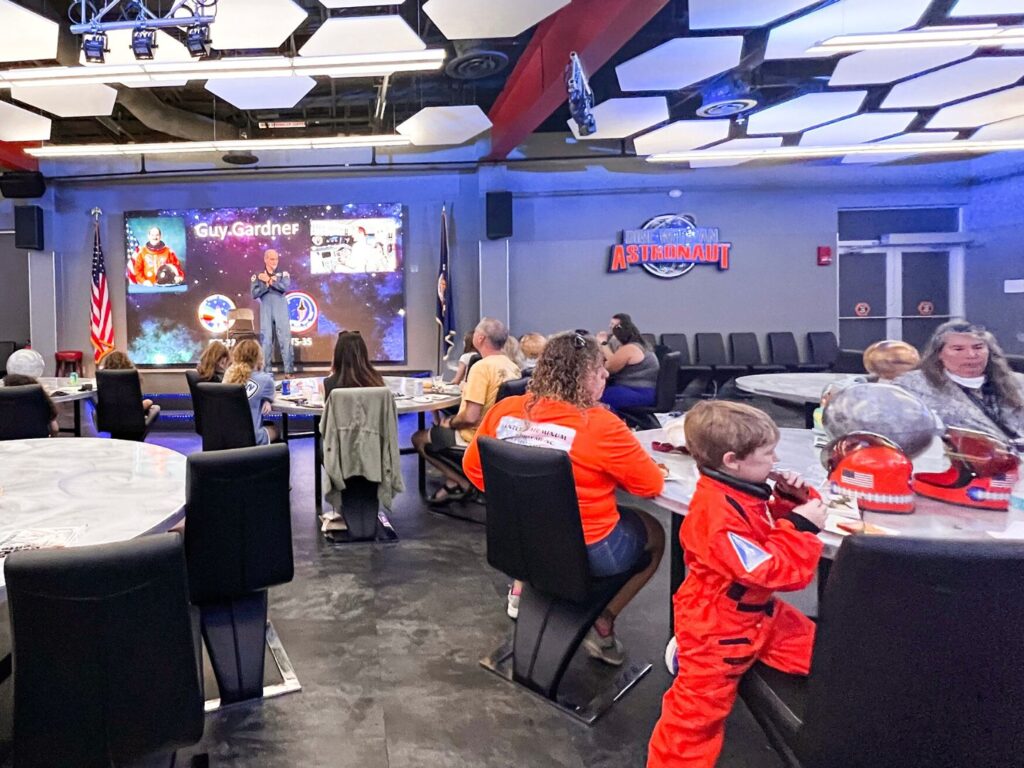 attendees of Chat with an Astronaut at Kennedy Space Center sit at round tables with chairs 