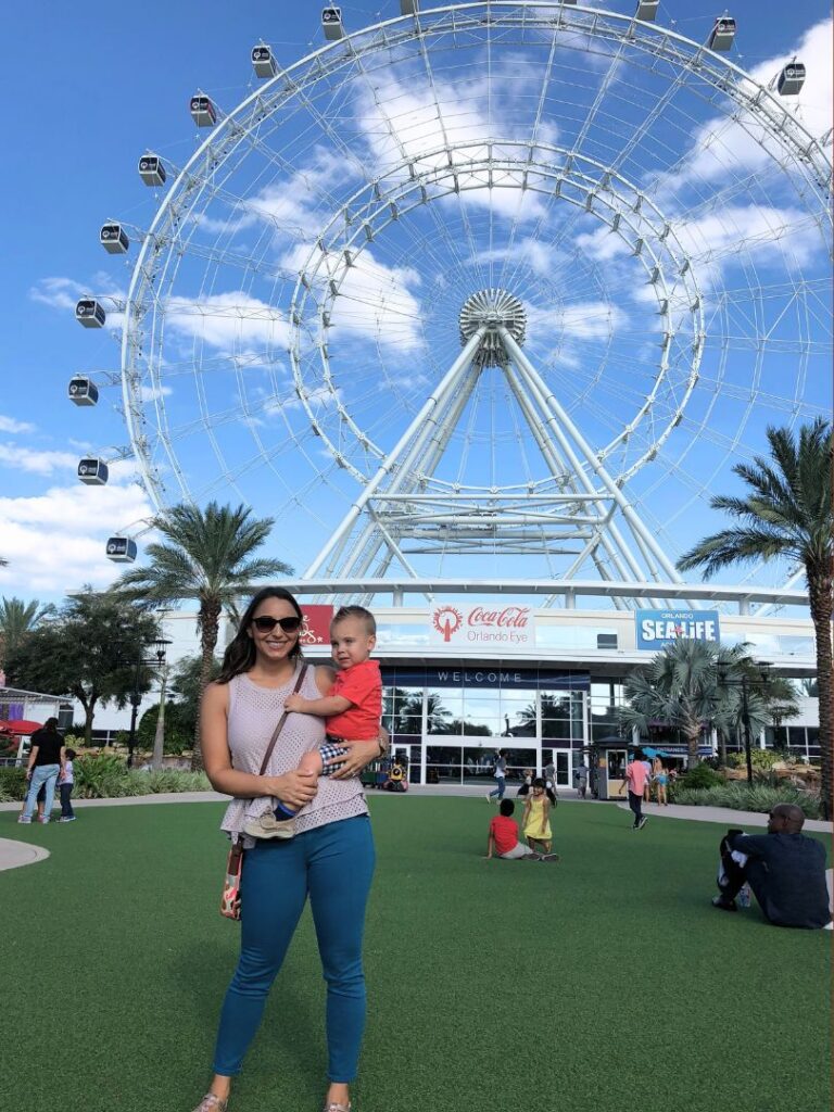 A woman and toddler child stand in front of The Wheel at ICON Park Orlando 