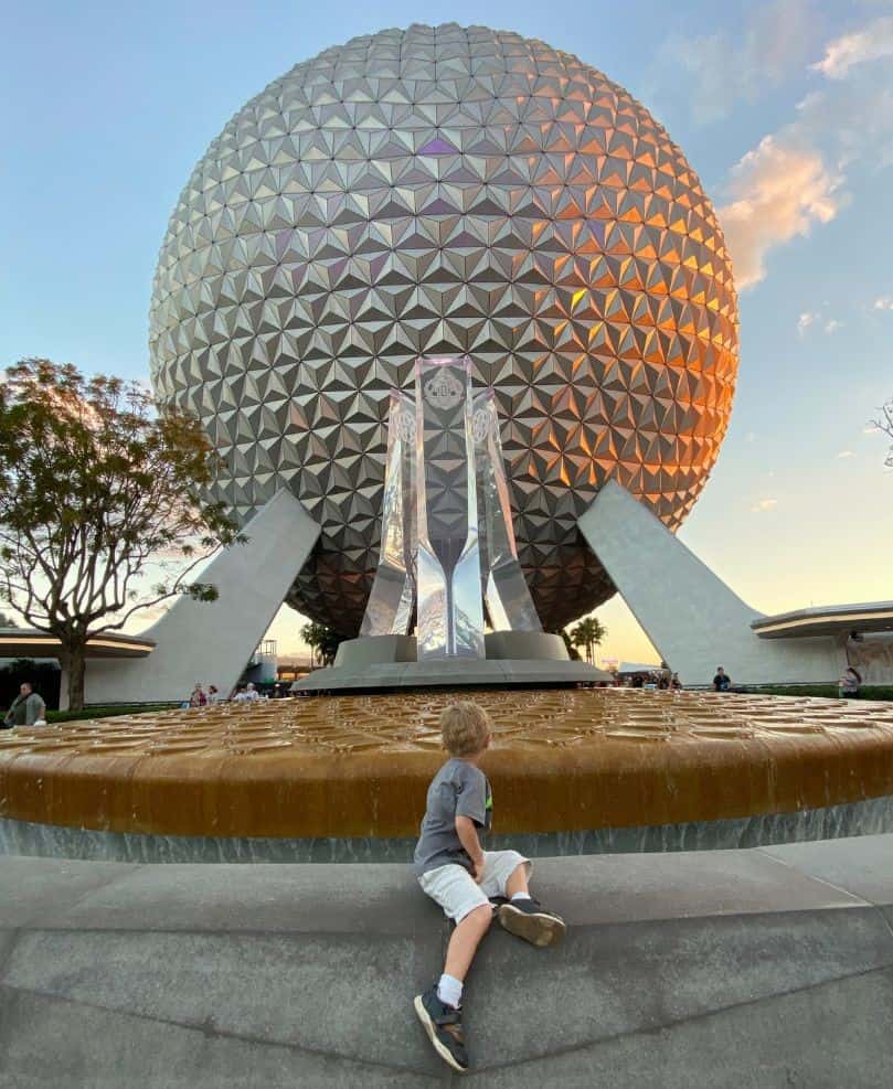 a young boy sits on a fountain Gazing at Spaceship Earth at EPCOT