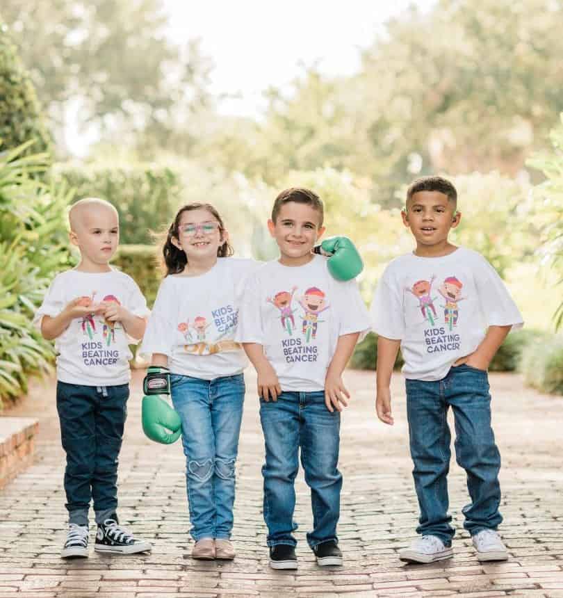 Group photo of four kids in jeans and wearing Kids Beating Cancer logo t-shirts 