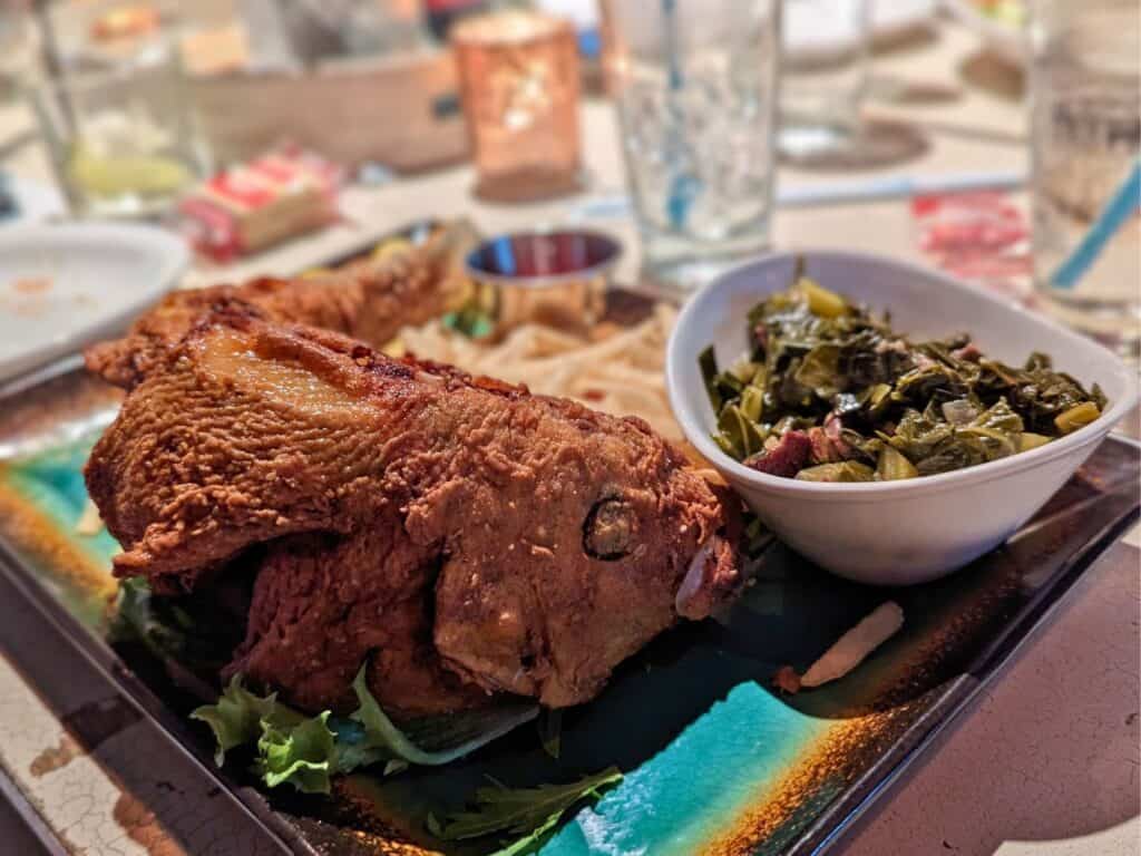 a whole fried fish with a side of collard greens at Reel Fish Coastal Kitchen in Winter Park, Florida