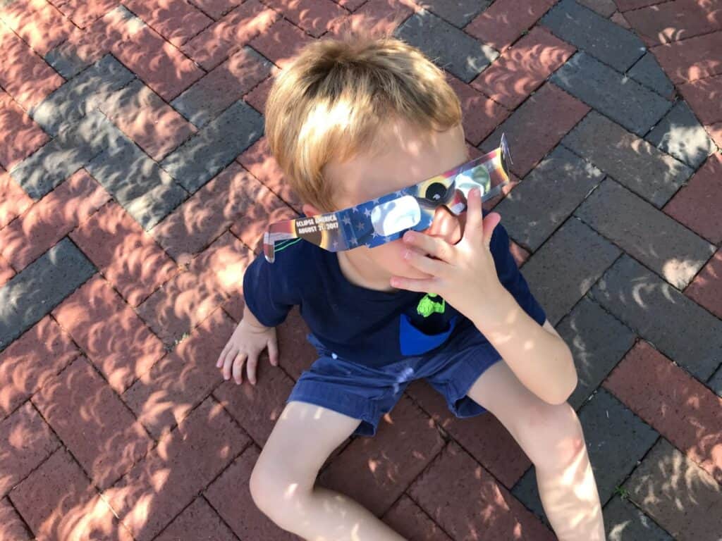 a young boy wears solar eclipse glasses and special shadows are created on the ground from the eclipse