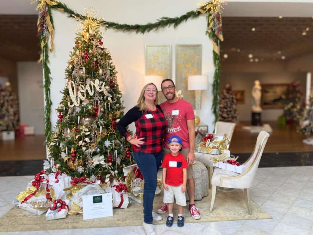 a family of 3 poses in front of a christmas tree during Festival of Trees Orlando Museum of Art