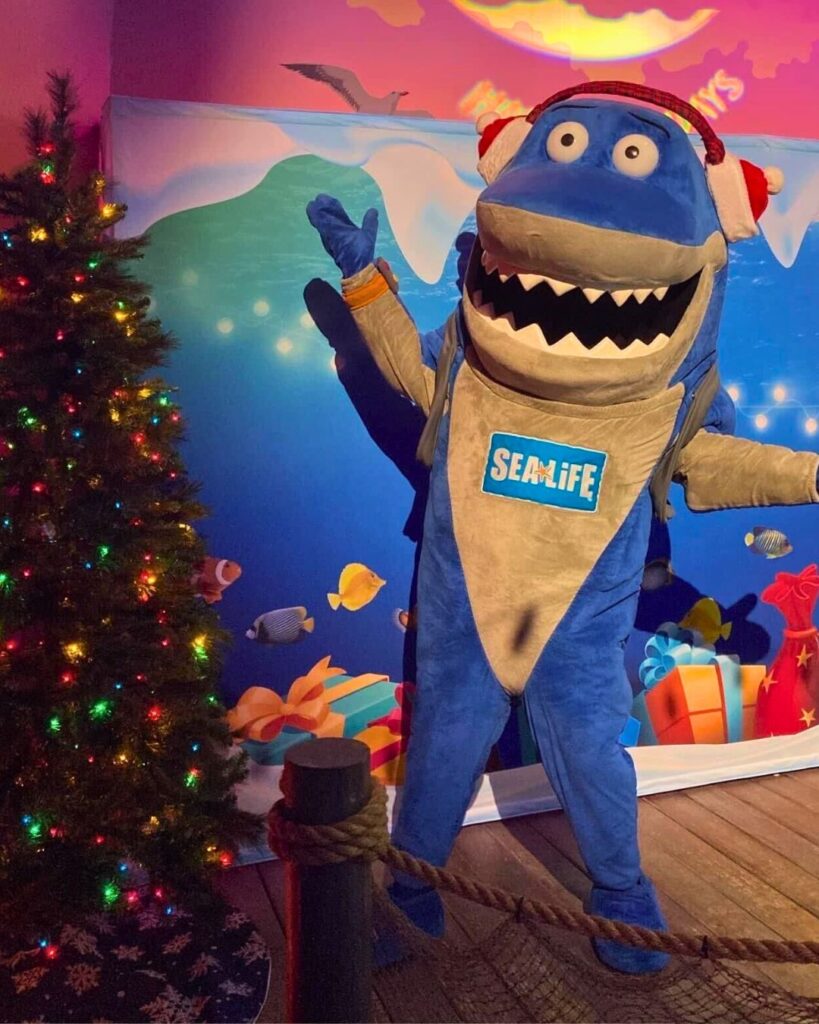 Sharky the SEA LIFE Orlando Mascot Wearing a Santa Hat and Standing Next to a Christmas Tree