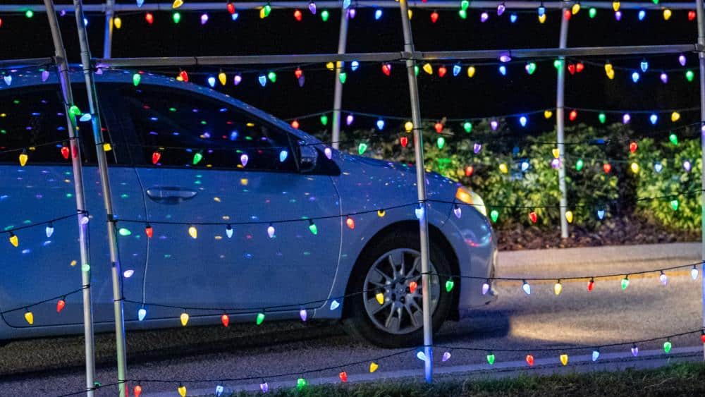 a white car drives through arches of christmas lights