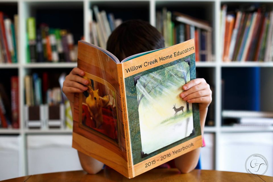 A Child holds a book titled Willow Creek Home Educators in front of his face