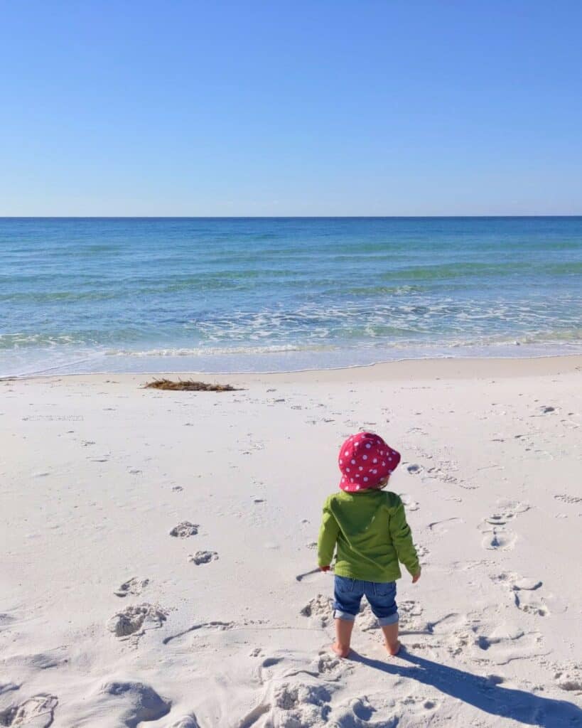 Image of a small child in a pink hat looking at the ocean at the beach at Topsail Hill Preserve State Park