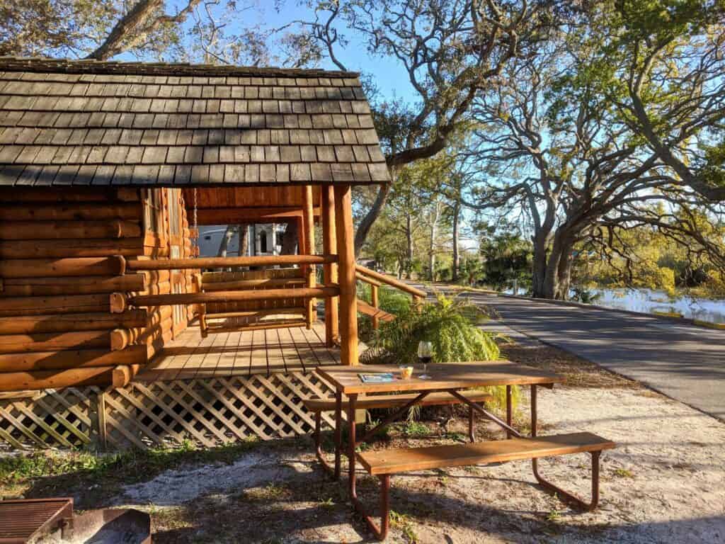 Image of the side of the outside of a St. Augustine’s KOA Cabin with trees and water in the background
