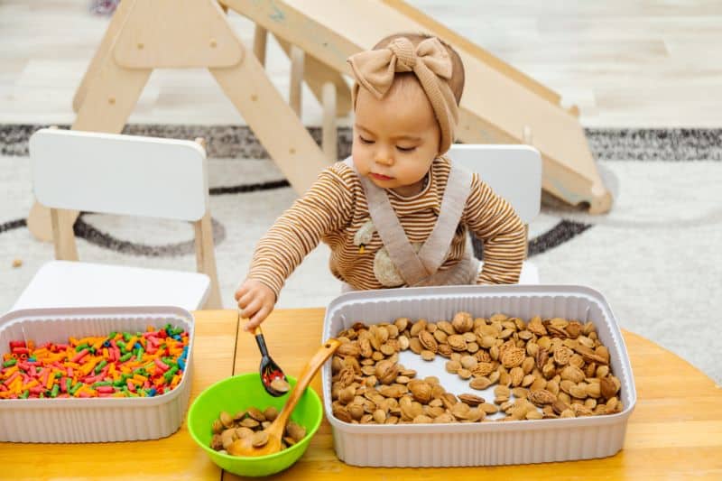 Busy Box Ideas for Toddlers young toddler with uncooked pasta walnuts and bowls - stock photo