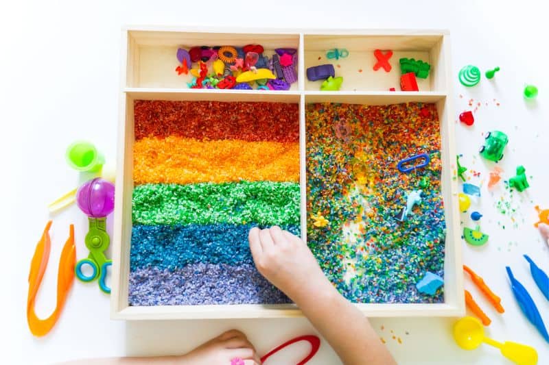 Sensory box with rainbow rice inside. Montessori material baby 