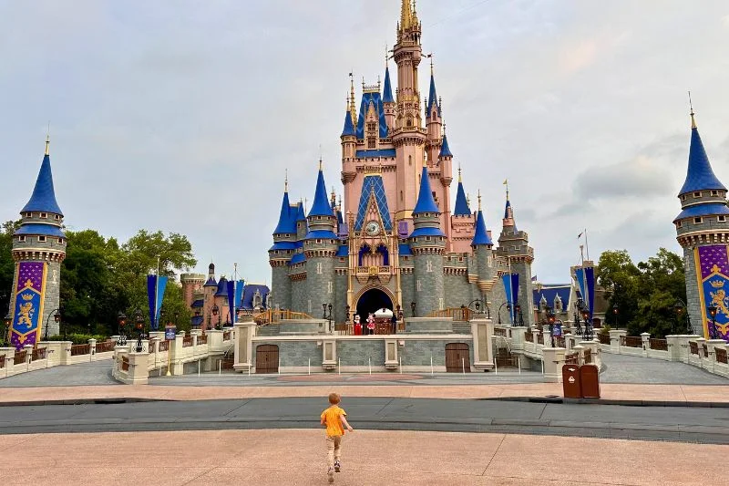 Young boy running toward Mickey and Minnie Mouse in front of Cinderella Castle at Magic Kingdom -