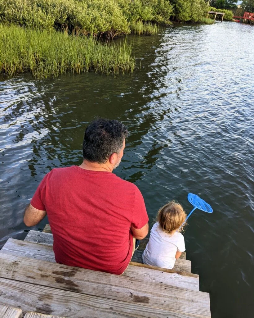 Man and small child sitting on a dock net fishing