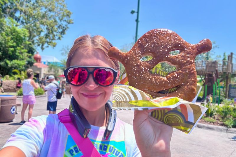 selfie style photo of a mom holding up the dreamworks land shrek pretzel shrekzel -