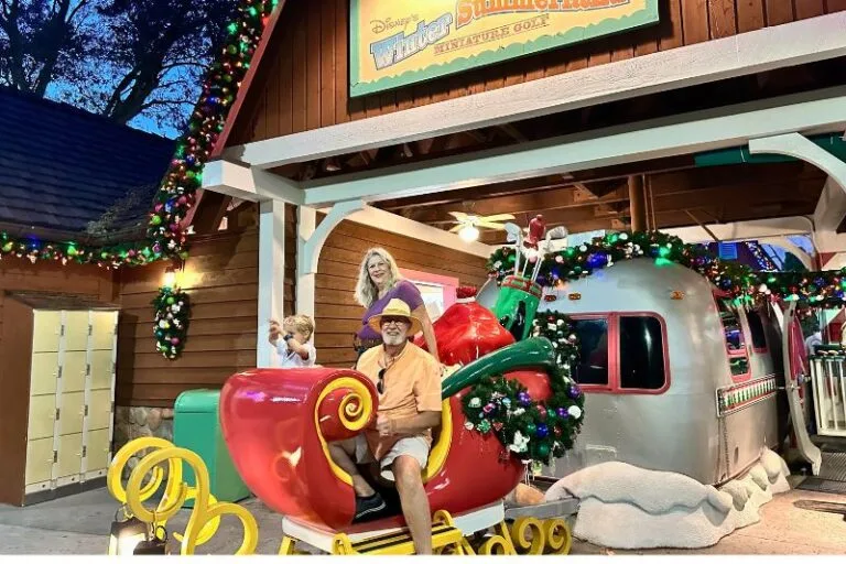 Affordable Disney Activities Winter Summerland Mini Golf grandparents pose with their grandson in Santa's sleigh -