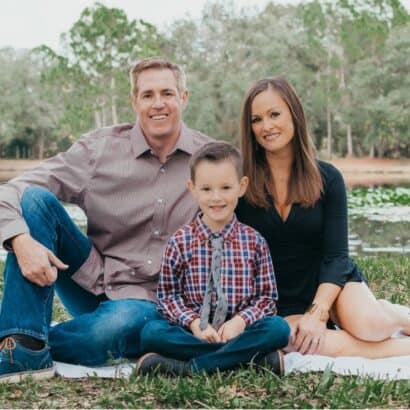 Brie Gorecki sitting outdoors with her family on a picnic blanket near a lake, smiling at the camera.