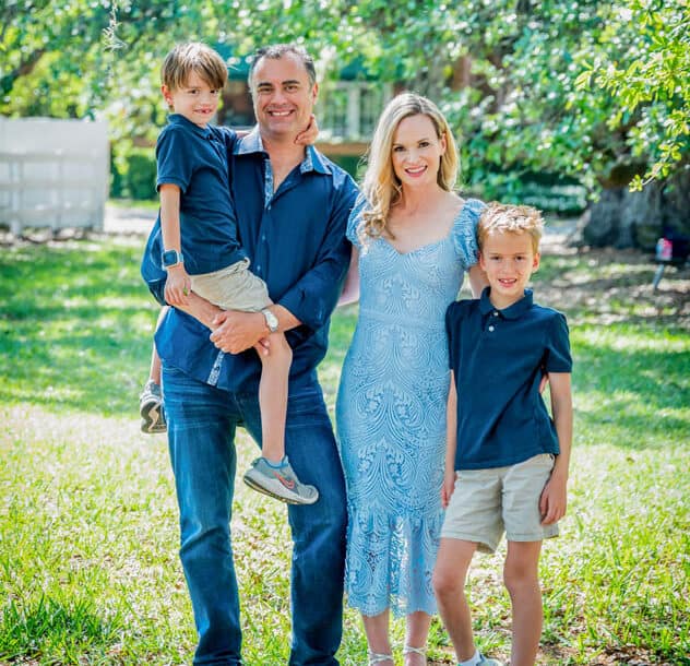 Laura Byrne with her husband and two young sons posing outdoors in a sunny, green park.