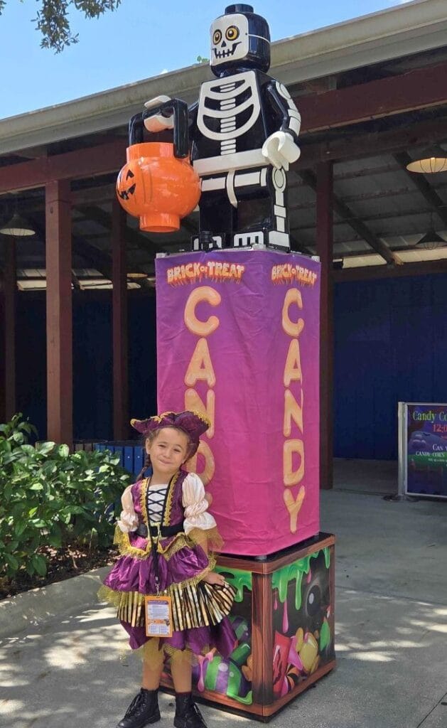 Young girl poses in front of LEGO Candy sign at LEGOLAND Florida Halloween - image by Zoe Joiner