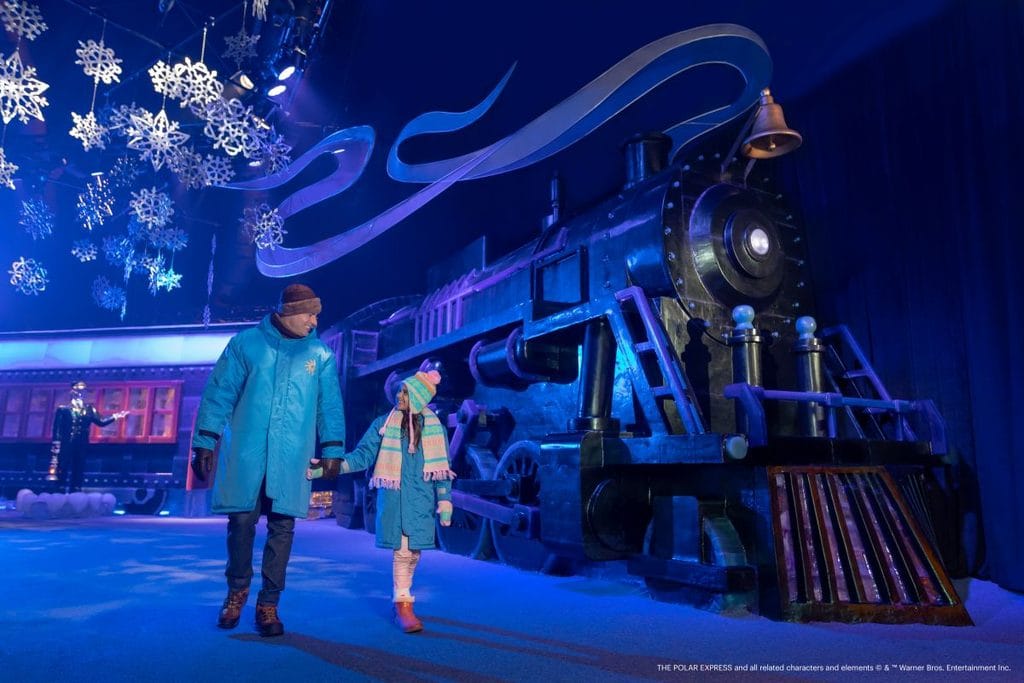 A girl holds hands with her Dad, walking next to the Polar Express Train car inside ice! at Gaylord Palms resort in Orlando