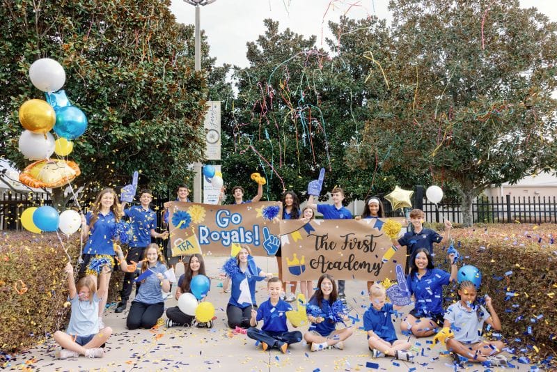 a large group of students of The First Academy celebrating with balloons and streamers
