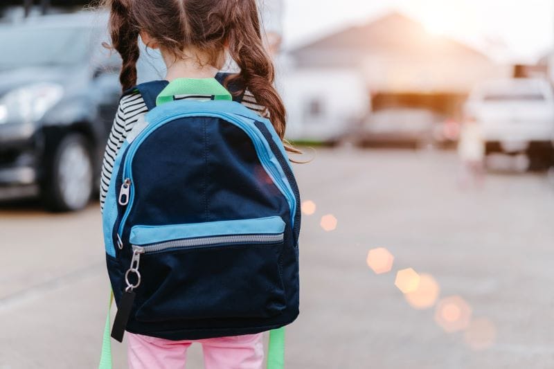 a young elementary school student wearing a backpack walks to school, showing the importance of choosing the right school program for your family