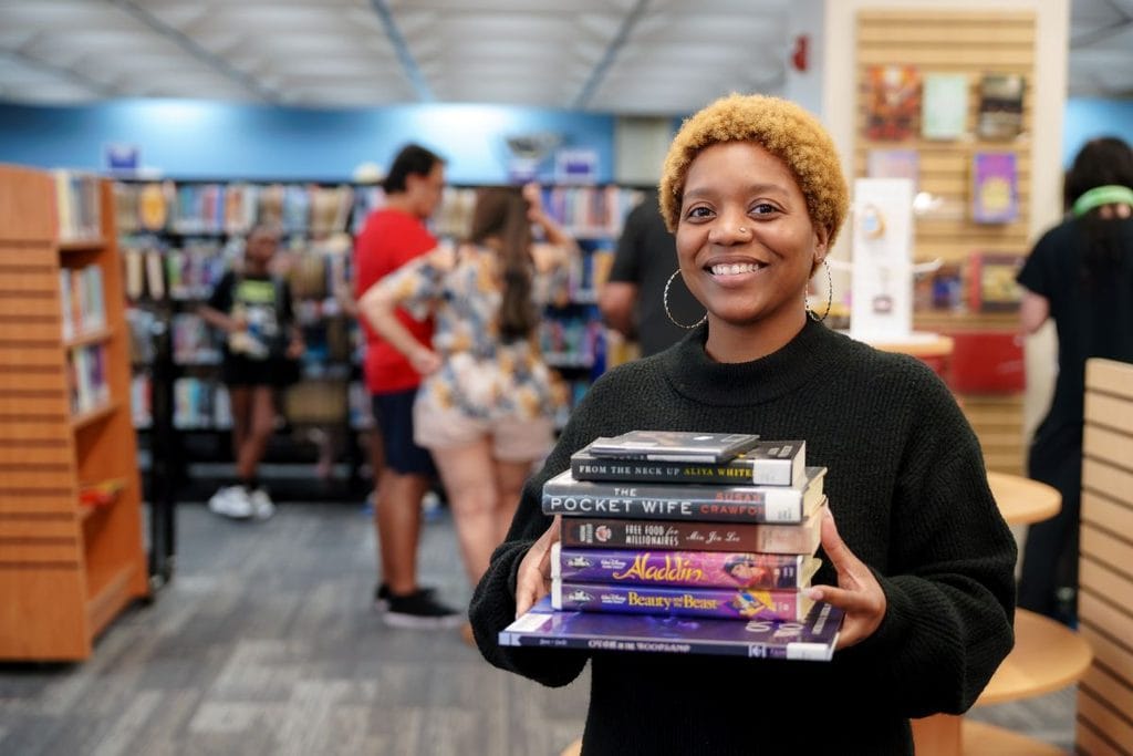 A woman carrying a stack of used movies at the Orange County Library Book Store 50% Off Sale in Orlando