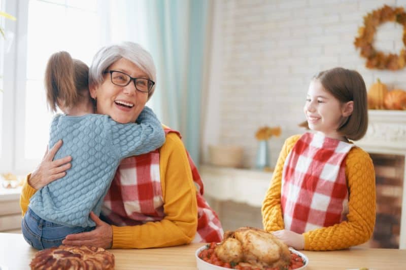 stock image of a grandmother hugging a child while wearing festive apron and thanksgiving decor in kitchen